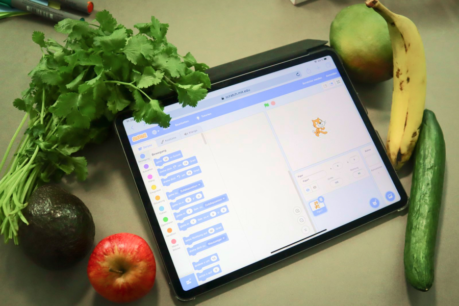 Ein Tablet, auf dem Scratch geöffnet ist. Um das Tablet herum liegt verschiedenes Obst und Gemüse