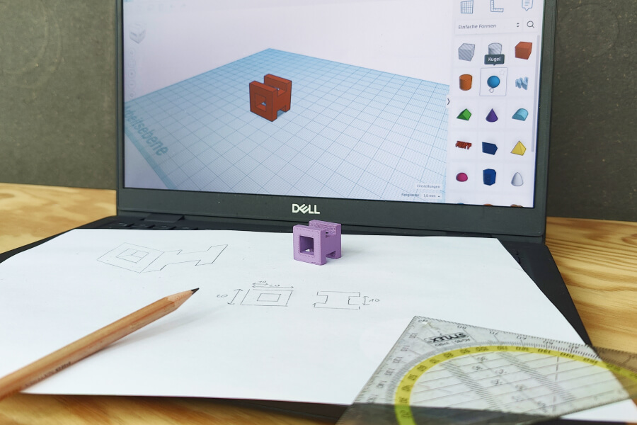 Ein Laptop mit Tinkercard, davor ein Stift, Papier mit Zeichnungen und ein 3D-Modell