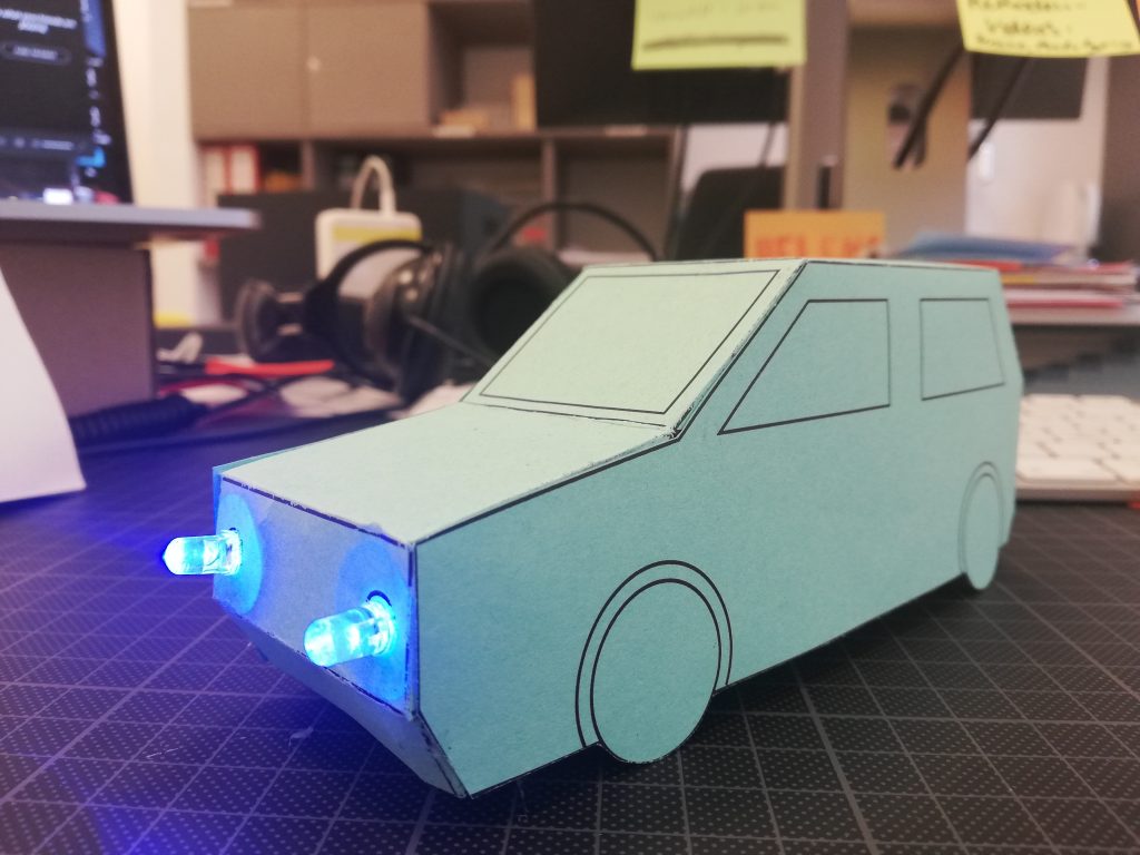 Ein Auto aus Papier, die Scheinwerfer sind leuchtende LEDs