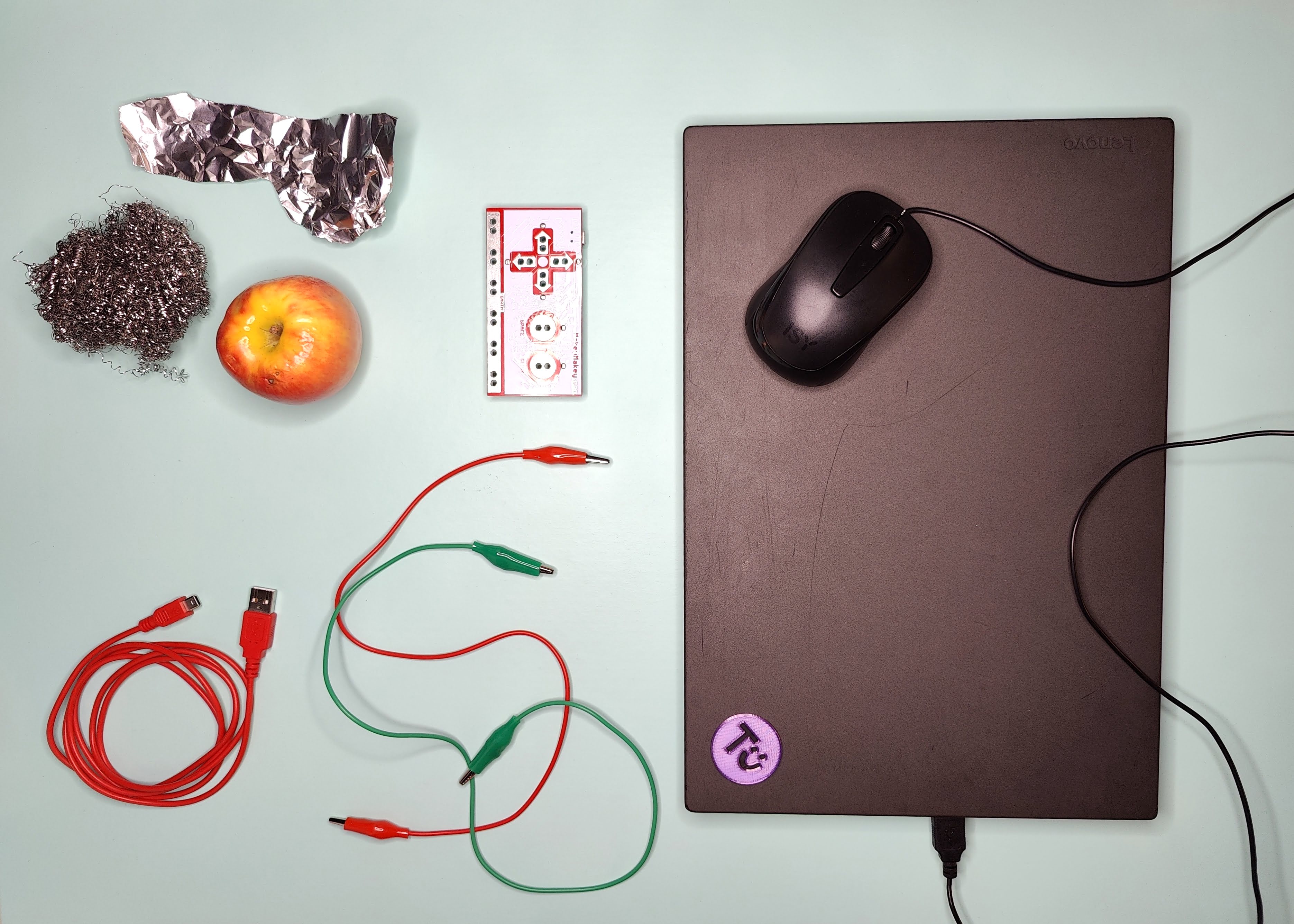 Laptop mit Maus, MakeyMakey, Leitende Objekte (Apfel, Stahlschwamm, Alufolie), 2 Krokoklemmen, USB-Kabel