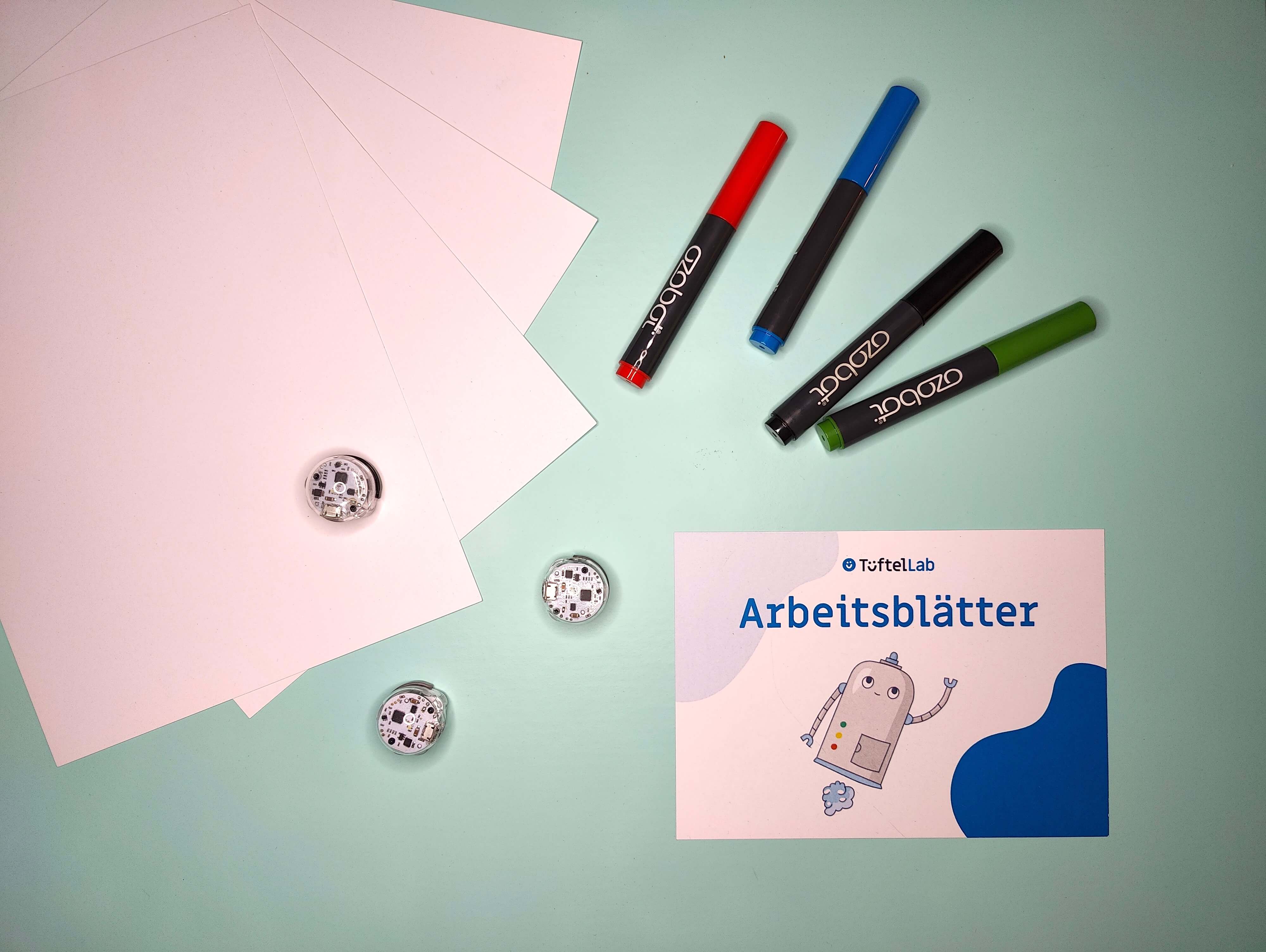 drei Ozobots, vier bunte Marker, ein paar Blatt Papier