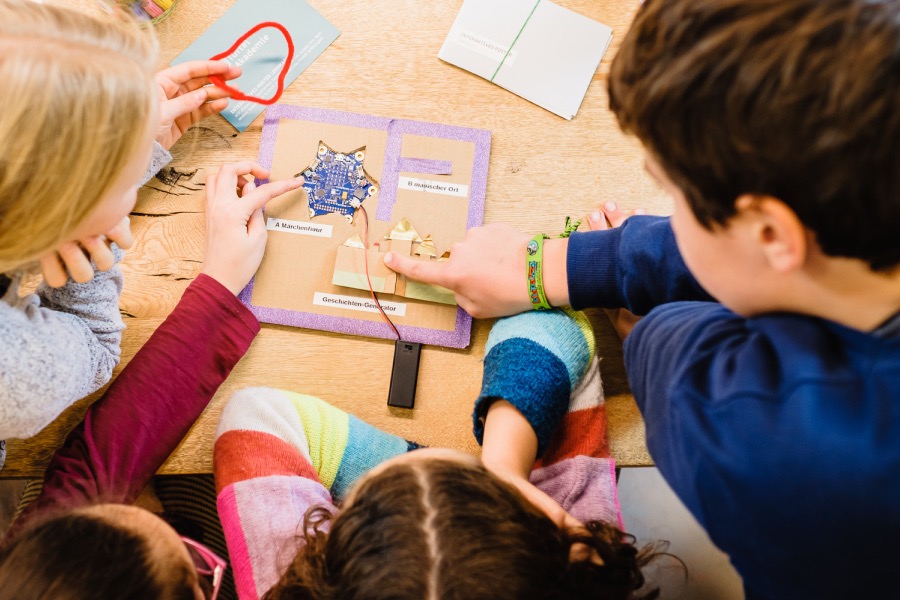 Mehrere Kinder sitzen um einen Tisch und arbeiten gemeinsam mit einem Calliope mini an einem gebastelten Projekt.