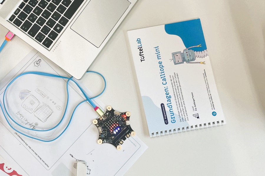 Ein Set Calliope-Lernkarten, daneben ein Calliope mini, der mit einem Laptop verbunden ist.
