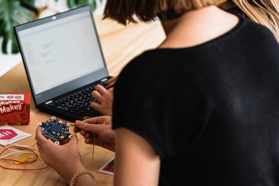 Zwei Personen sitzen vor einem Laptop, eine hält einen Calliope mini in den Händen