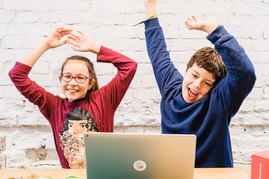 Zwei Kinder sitzen vor einem Computer und jubeln