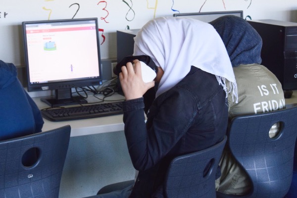 Ein Mädchen sitzt vor einem Computer. Sie schaut in eine VR-Brille.