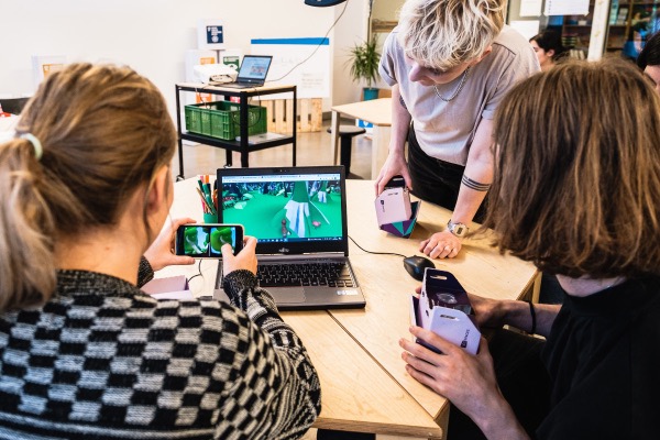 Drei Personen beugen sich über einen PC, auf dem Delightex geöffnet ist. Eine der Personen hält ein Smartphone vor den PC.